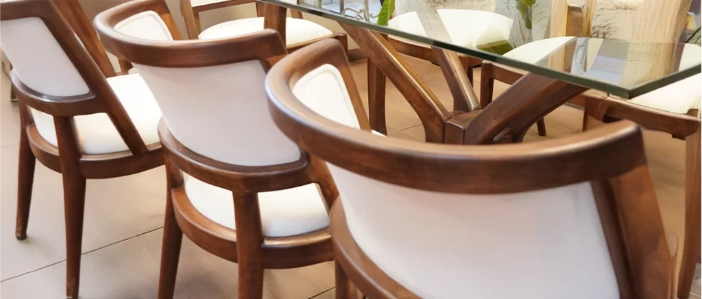 Vista de comedor con mesa de vidrio y sillas de madera tapizadas, representando elección funcional y elegante.